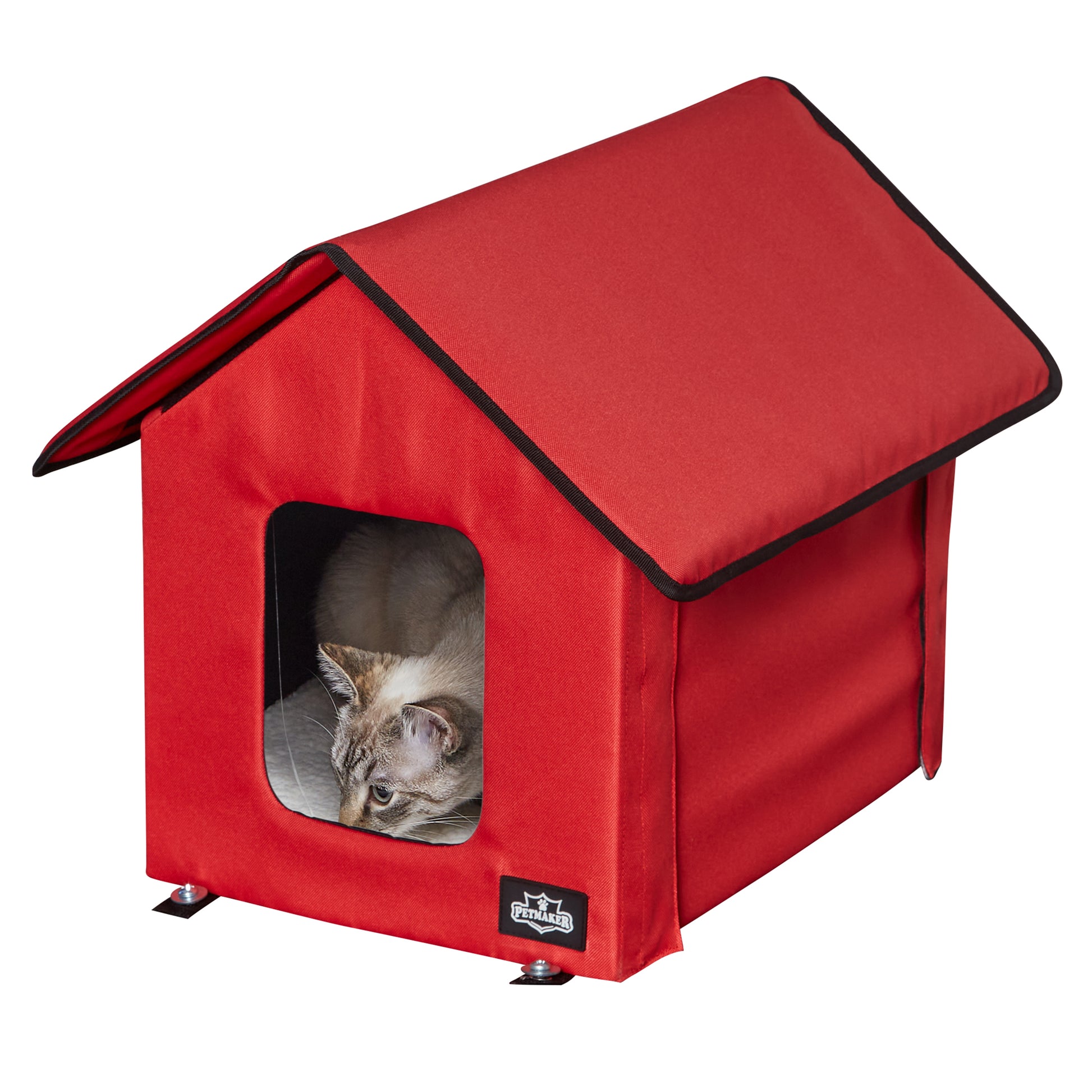 Siamese cat has nose down toward the front door of a red pet house while the cat prepares to pounce on the happenings outside of the pet house. 